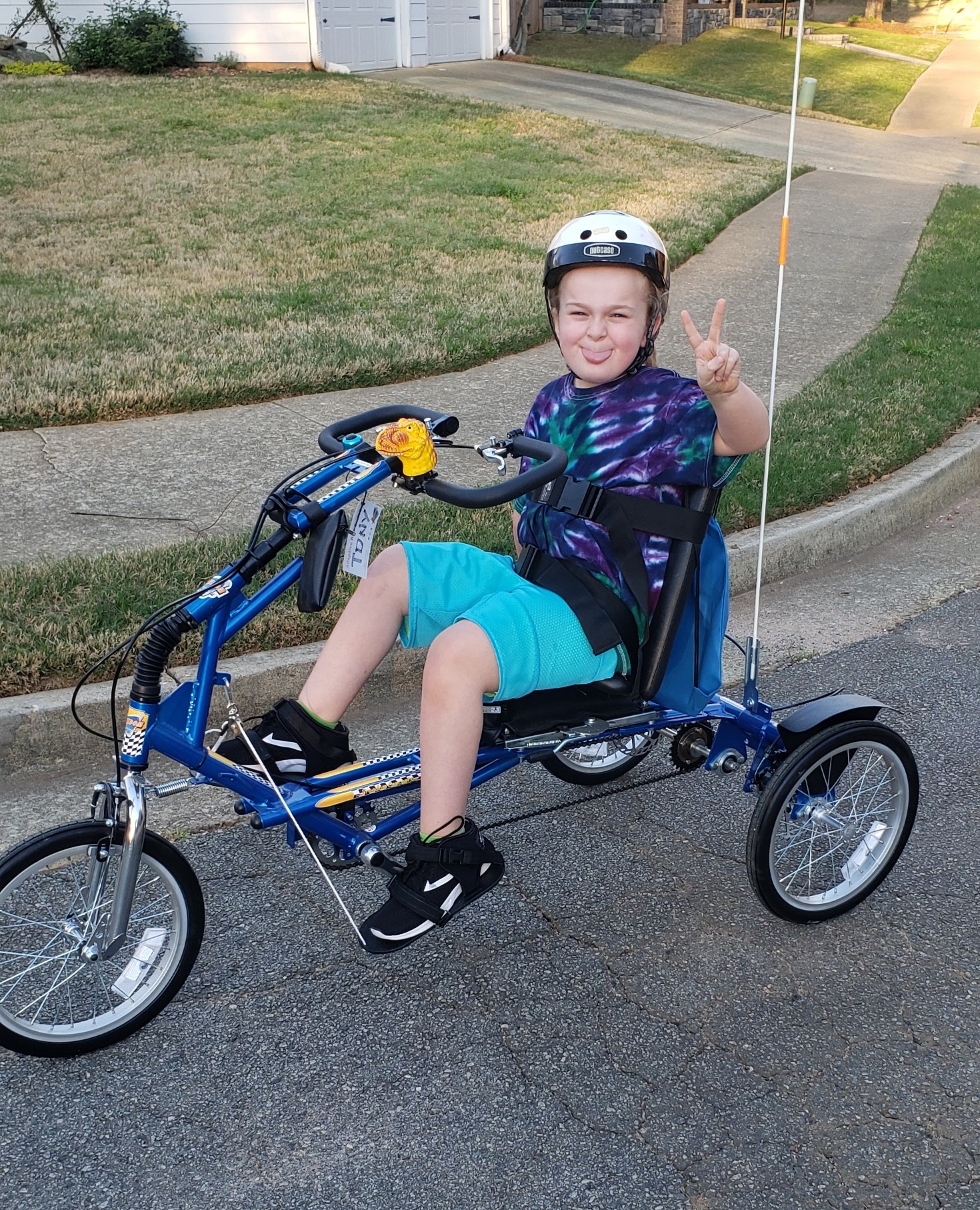 Ayden sitting on his adaptive bike making a peace sign with his hands. 